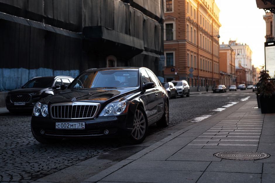 A luxurious black Maybach car parked on a cobblestone street in an urban setting at sunset