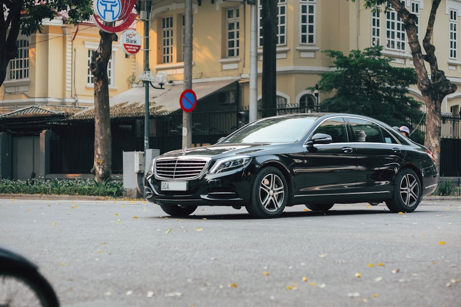 A sleek black sedan navigates an urban street lined with historic buildings and lush trees