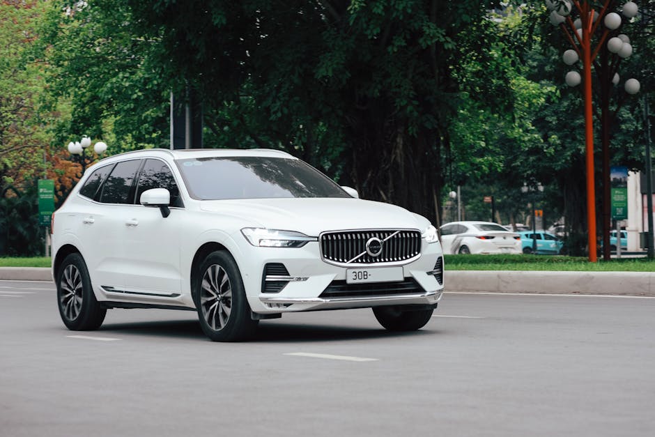 A sleek white SUV driving on a city road surrounded by greenery.