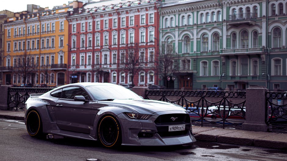 A sleek grey sports car parked on an urban street with colorful historic buildings in the background